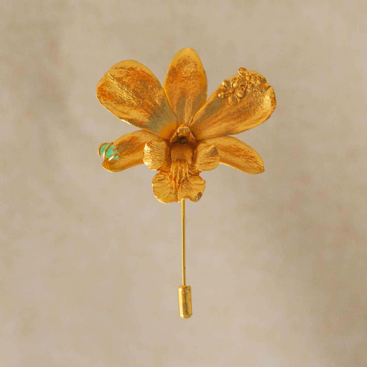 Broche dorado artesanal de orquídea Dendrobium con esmeralda