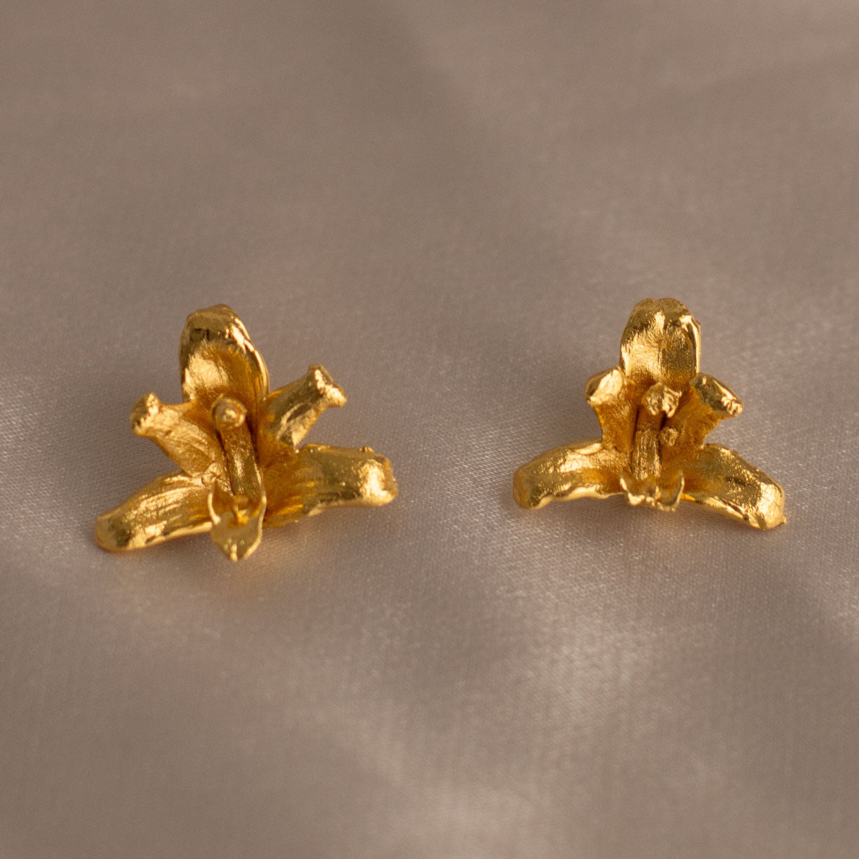 Aretes artesanales de Orquidea Maxilaria inmortalizada en bronce con baño en oro, mostrando detalles únicos de la flor