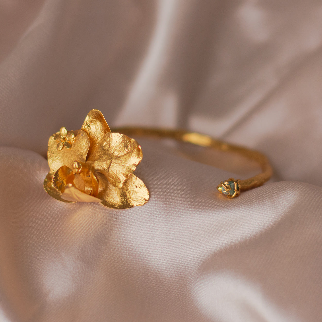 Brazalete Orquídea Phalaenopsis Baby Esmeralda en bronce bañado en oro de 24k, destacando la belleza única de las orquídeas y ramas inmortalizadas con detalles de esmeralda colombiana