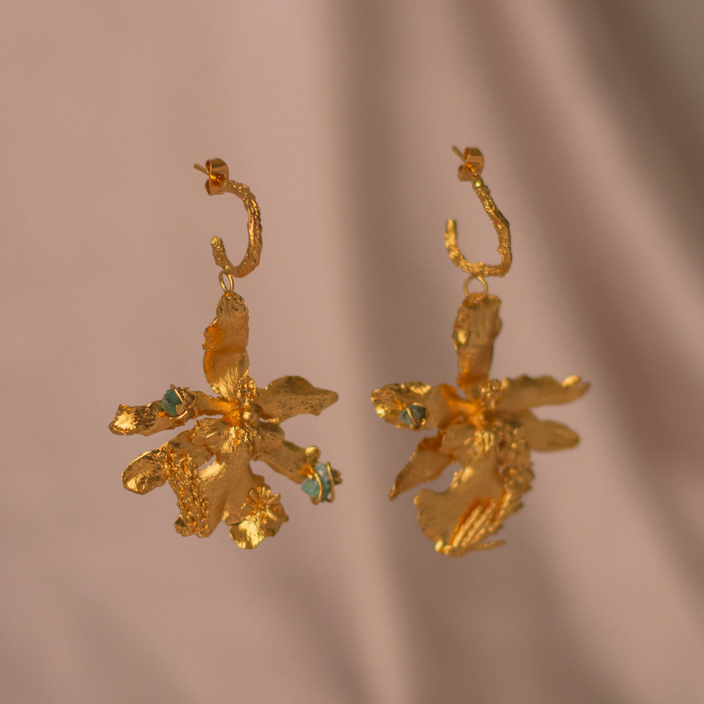 Aretes Candonga Orquidea Odontoglossum Pino Esmeralda en bronce bañado en oro de 24k, destacando la belleza única de las flores y hojas inmortalizadas con detalles de esmeralda.