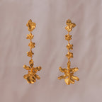 Aretes Orquídea Chocolate Hortensia Sauco en bronce bañado en oro de 24k, destacando la fusión de tres flores naturales inmortalizadas.
