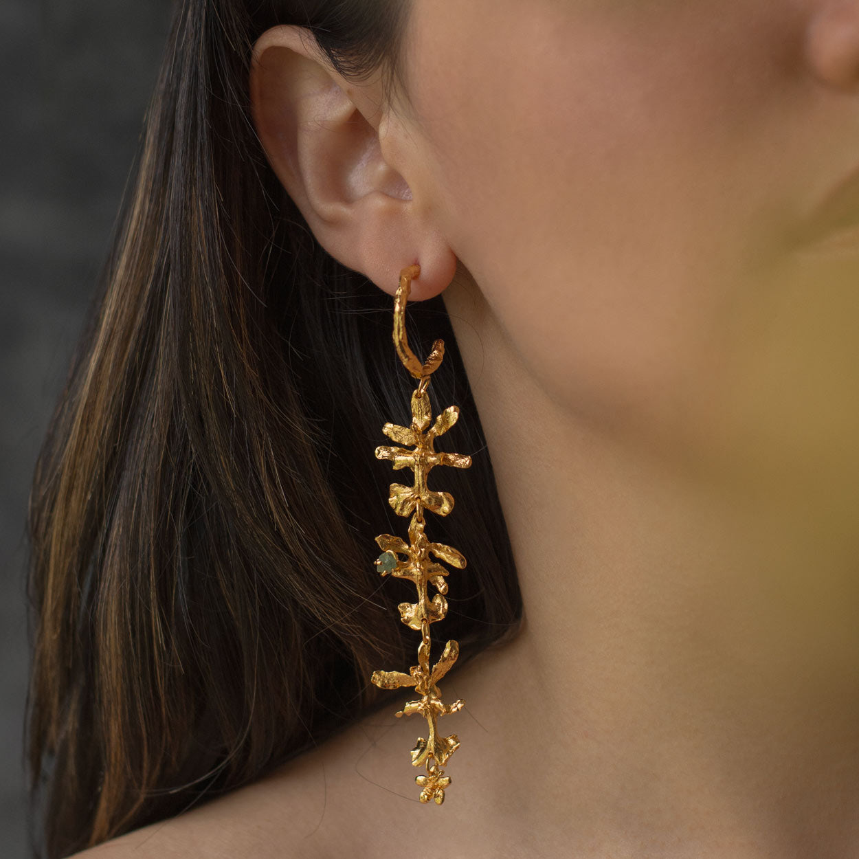 Aretes Aro Candonga Tres Orquídeas Oncidium Esmeraldas en bronce bañado en oro de 24k, adornados con morralla de esmeralda colombiana, mostrando la belleza natural de las orquídeas oncidium y las ramitas de palma inmortalizadas