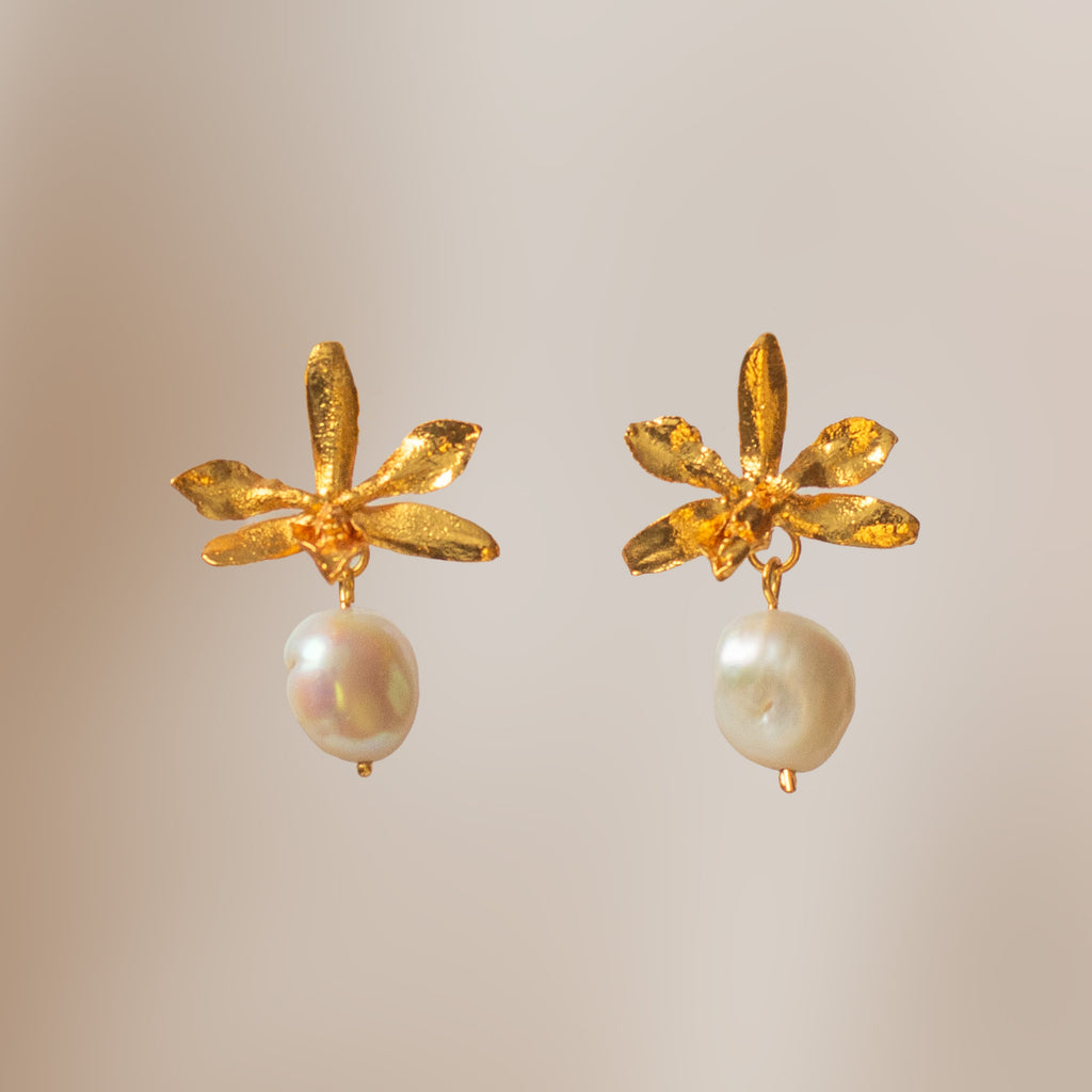 Aretes tipo topo dorados con forma de orquídea Prosthechea Sceptra real y una perla blanca colgante de forma irregular.