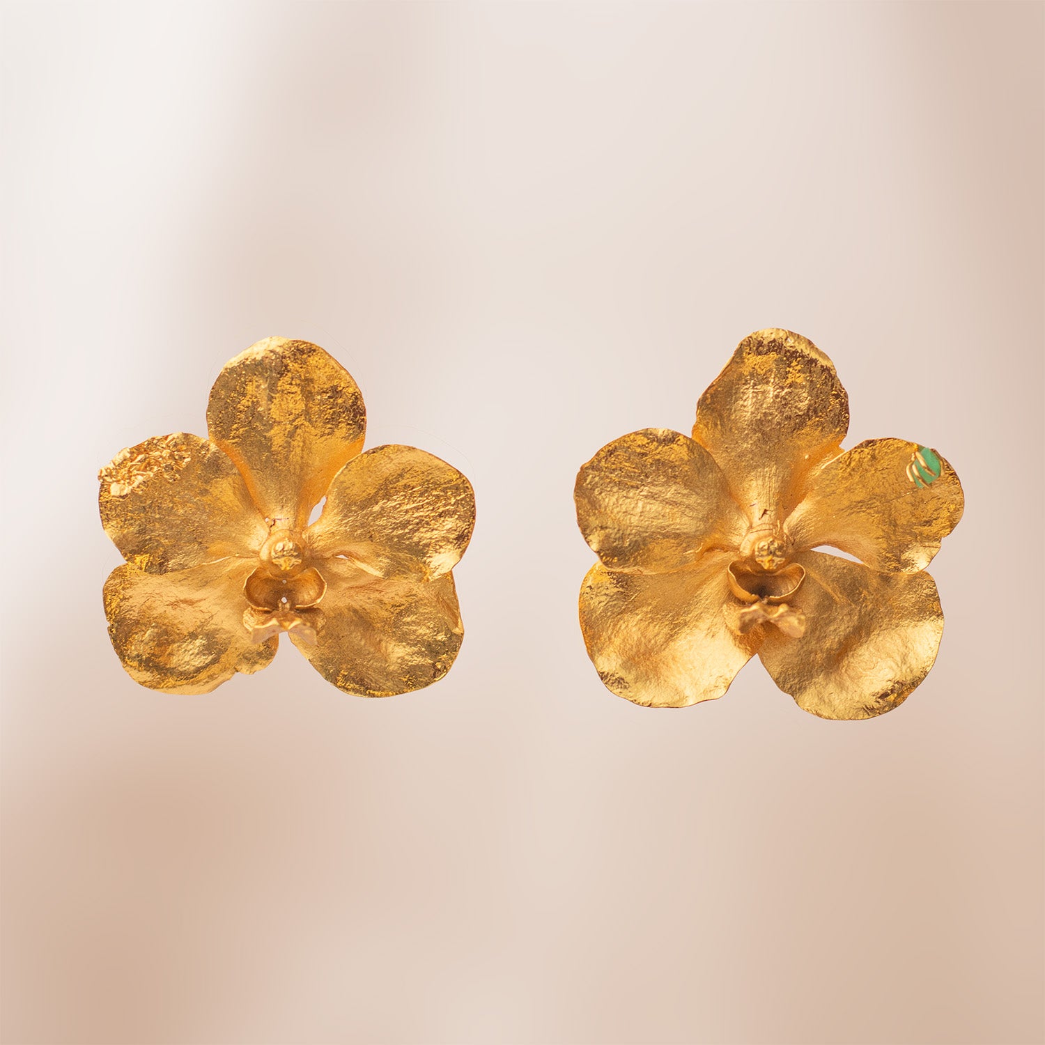Par de aretes grandes dorados con forma de orquídea Vanda real, mostrando una pequeña esmeralda verde en uno de sus pétalos.