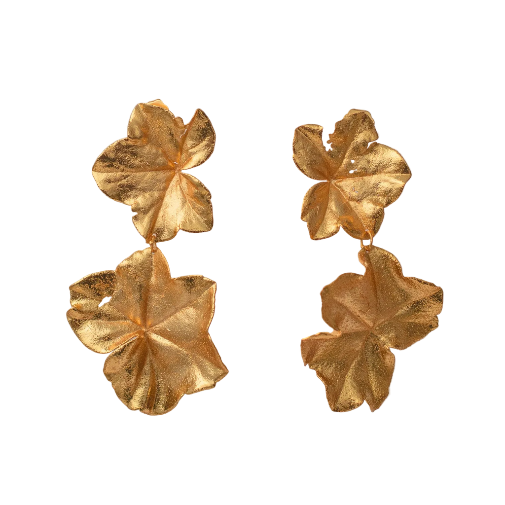 Par de aretes dorados largos compuestos por dos hojas de hiedra unidas verticalmente, mostrando texturas y agujeros naturales de la planta.