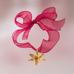 Collar con gran lazo de organza color magenta que sostiene un dije de orquídea real dorada con una pequeña esmeralda incrustada.