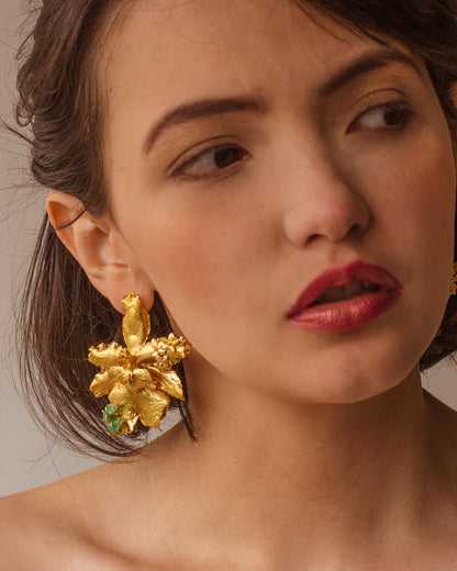 Mujer usando unos aretes en flor de orquidea odontoglossum natural inmortalizada con detalles en flores de sauco y esmeraldas colombianas. Acabado en oro de 24 kilates