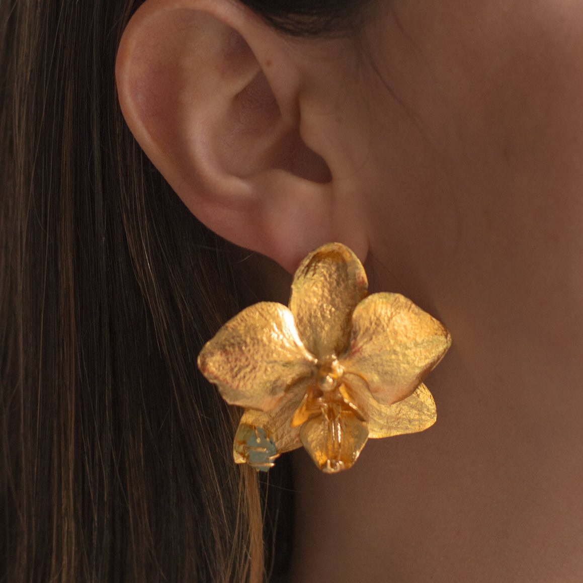 Modelo con Aretes de orquidea phalaenopsis inmortalizados en una joya con esmeralda