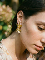 Detalle de aretes florales elegantes, orquídea andina preservada en oro con diseño de movimiento natural.