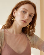 Modelo usando aretes de orquídea Encyclia oncidioides real con cadenas largas doradas en movimiento — joyería botánica Colombia, fundición orgánica, Liz de la Cruz
