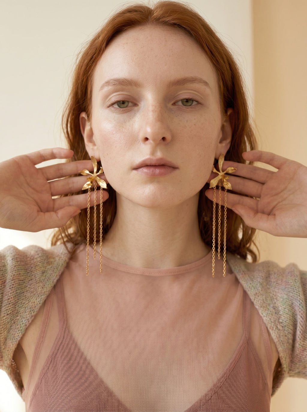 Modelo sosteniendo aretes colgantes de orquídea silvestre colombiana inmortalizada en oro 24k con tres cadenas finas, joyería botánica Bogotá, Liz de la Cruz
