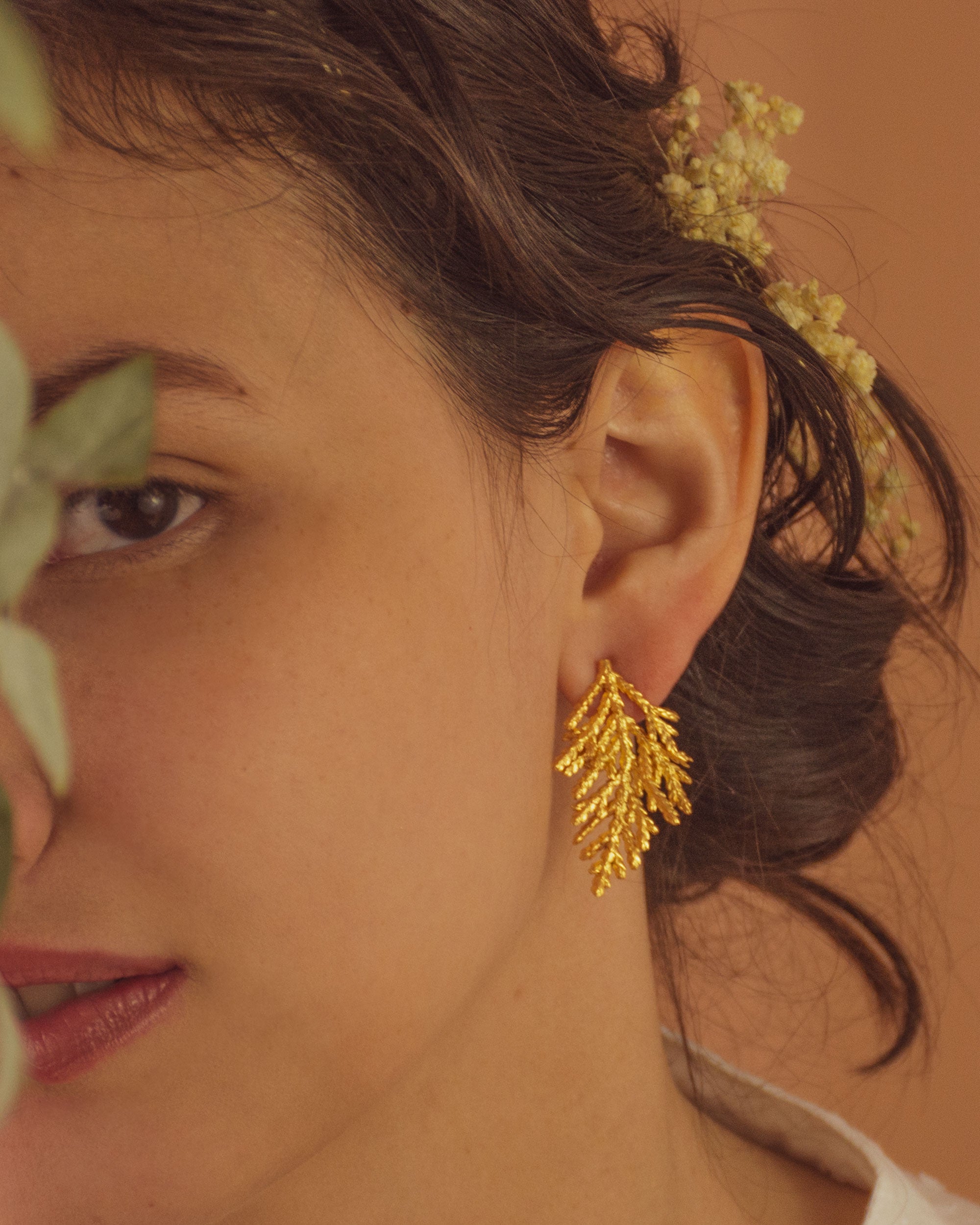 Joyería artesanal de aretes topo con hoja de pino inmortalizada en oro de 24k