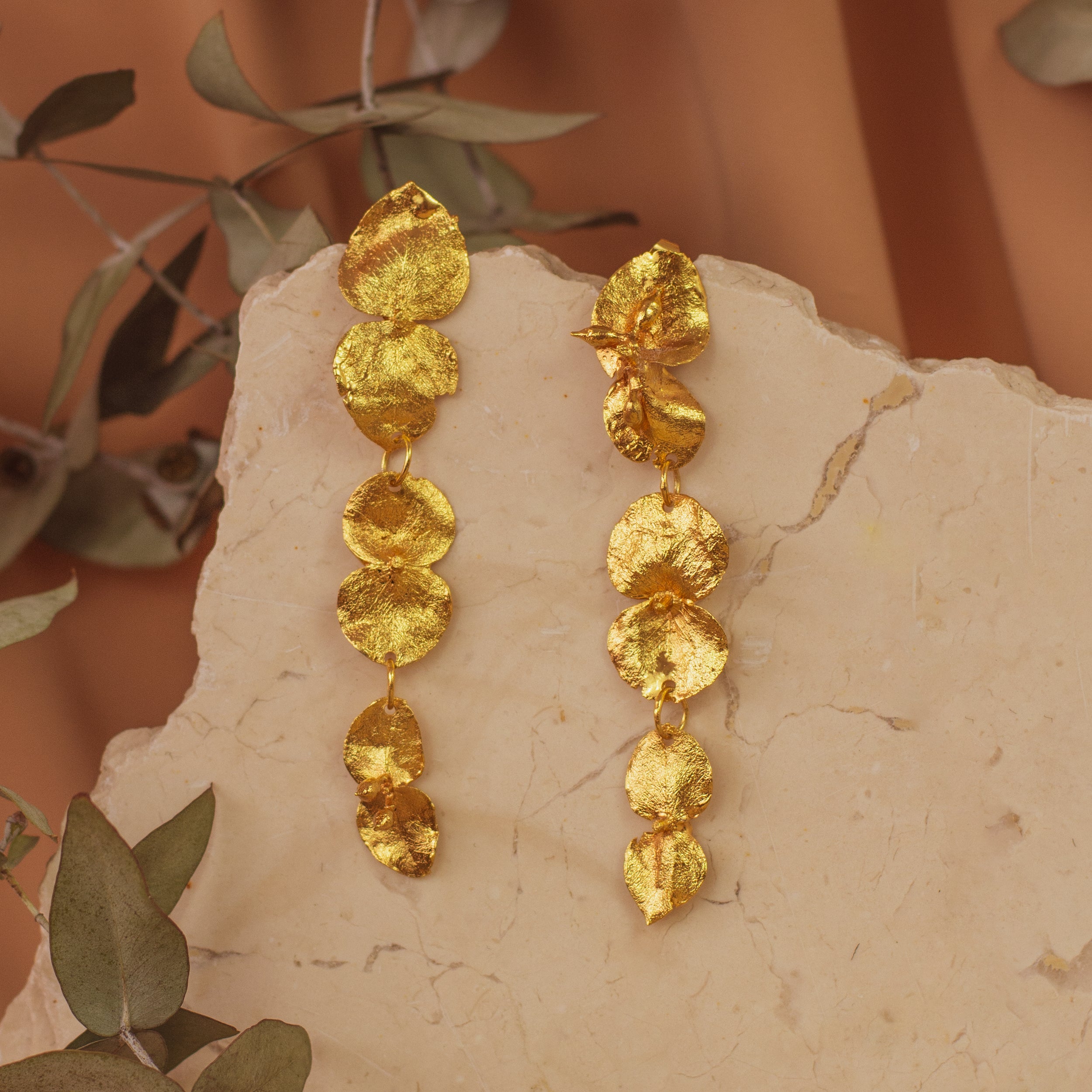Aretes Largos Tres Eucaliptos en bronce bañado en oro de 24k, resaltando la delicadeza y el diseño único de las hojas naturales