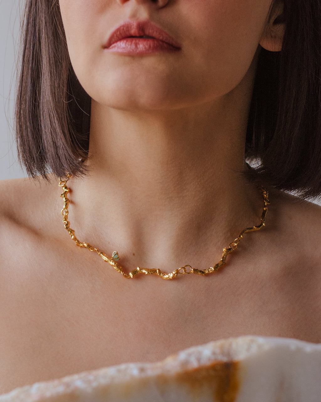 Collar Choker Ramita Palma Coco Esmeralda en bronce bañado en oro de 24k, destacando la textura natural de la ramita y el brillo verde de las esmeraldas