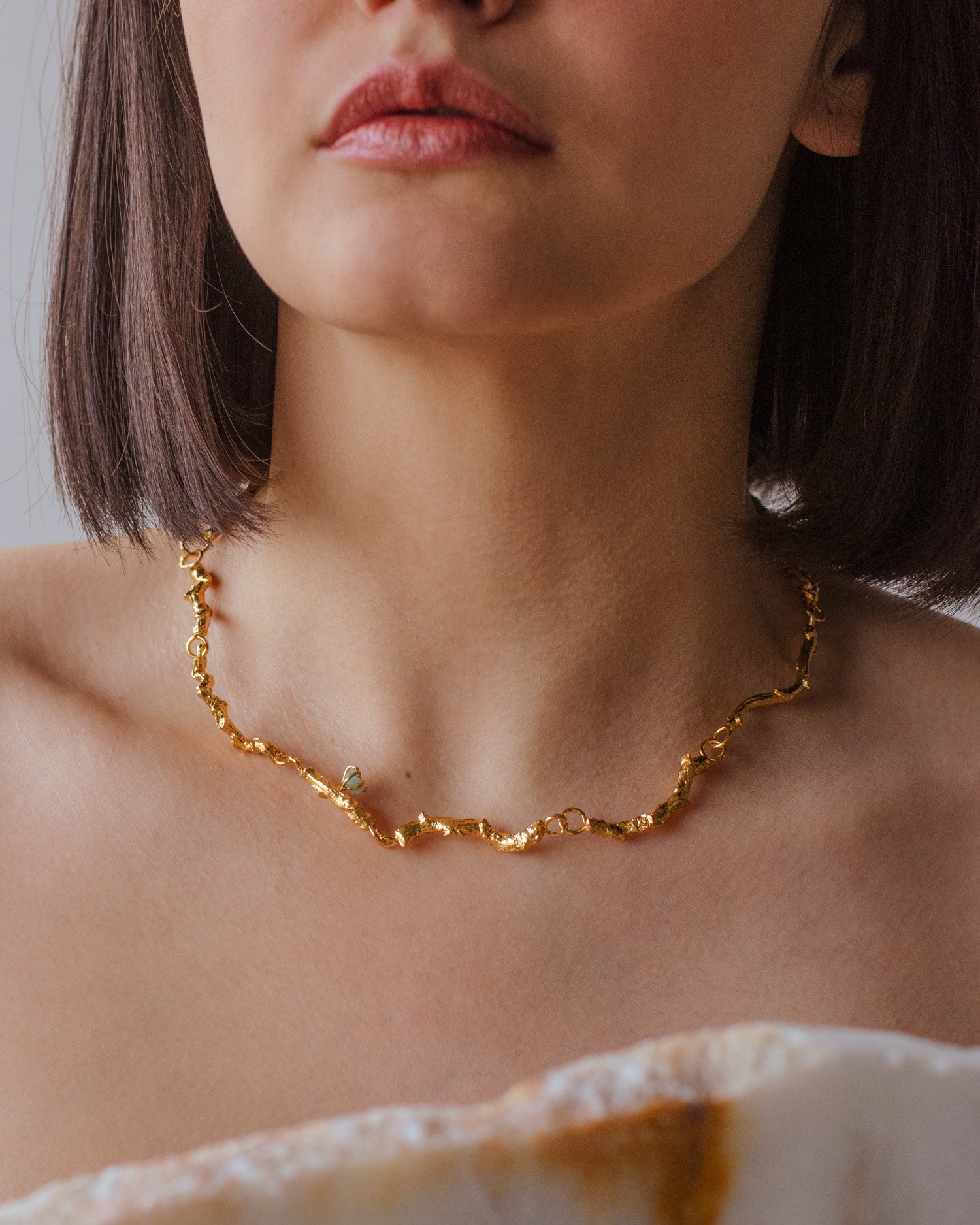 Collar Choker Ramita Palma Coco Esmeralda en bronce bañado en oro de 24k, destacando la textura natural de la ramita y el brillo verde de las esmeraldas