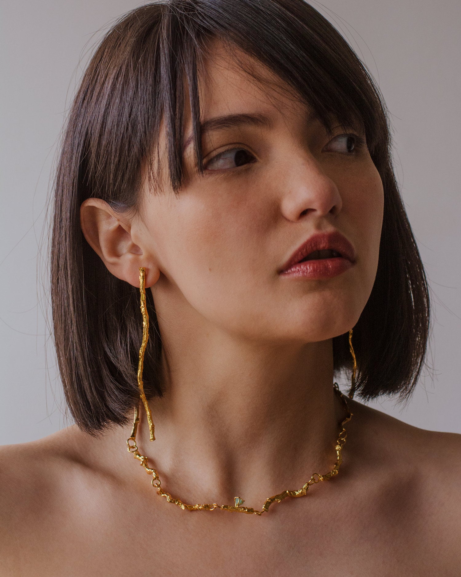 Collar Choker Ramita Palma Coco Esmeralda en bronce bañado en oro de 24k, destacando la textura natural de la ramita y el brillo verde de las esmeraldas